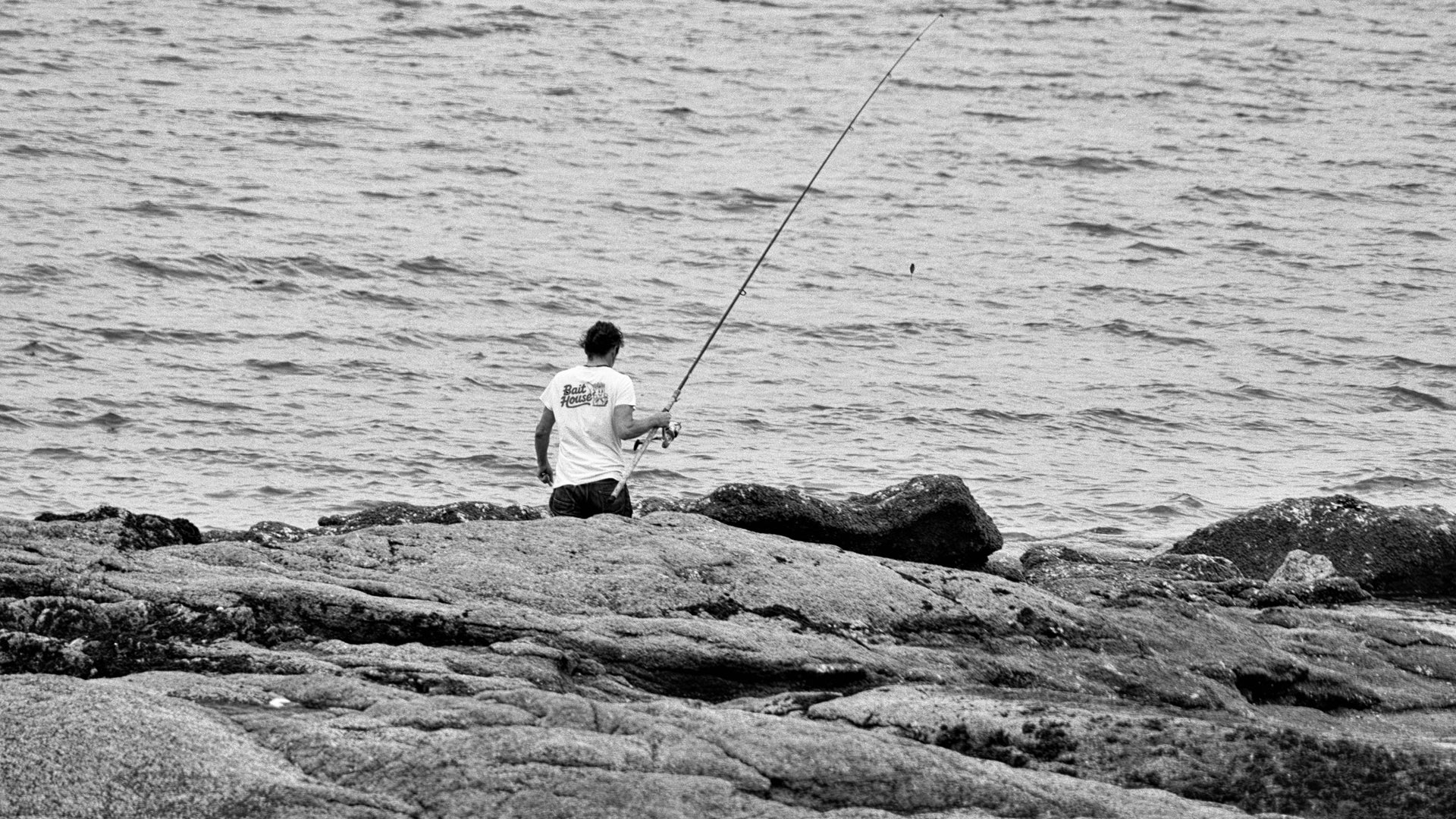 Person fishing on rocks by the water